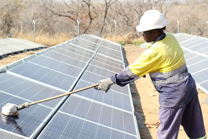 A technician cleaning a photovoltaic array in the sun